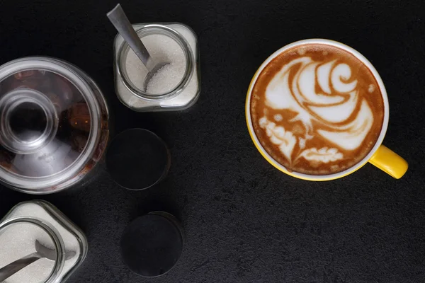 Copa de capuchino y tazones de azúcar sobre fondo negro. Arte latte —  Fotos de Stock