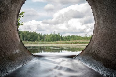 Perfect view from concrete drain pipe in the forest river. Slow water flow from the lake. clipart