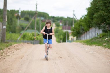 Tepe çakıl yolunda scooter süren bir çocuk. Kırsalda oynayan küçük kız.