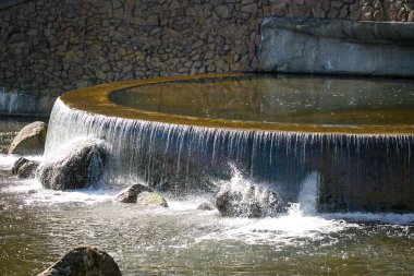 Şehir nehrinde küçük güzel bir şelale. Arka planda doğal taş duvar var..