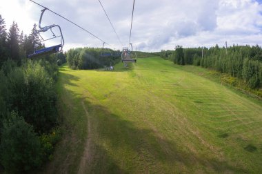 Güneşli yaz sezonunda boş kayak asansörü. Yeşil çimenler, ağaçlar ve bulutlu gökyüzü, yüksek bir yerden manzara..