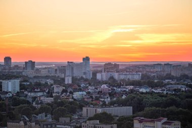 Gün batımında büyük bir şehrin manzarası. Minsk şehrinin manzarası. Renkli kırmızı gökyüzü, birçok farklı ev ve şehrin sokaklarında yeşil ağaçlar..