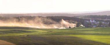 Belarus 'un kırsal kesiminin panoraması. Tarım alanları görüşü. Taze yeşil alan ve küçük bir Avrupa kasabası. Yanmış otlardan çıkan duman tüm alana yayılır. Arka planda sisli büyük bir orman