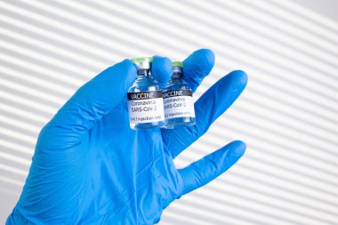 Coronavirus COVID-19. Tek dozda deneysel aşı içeren şişeler. Lateks eldivenli bilim adamının eli iki şişeyi tutuyor. Tıp konsepti.