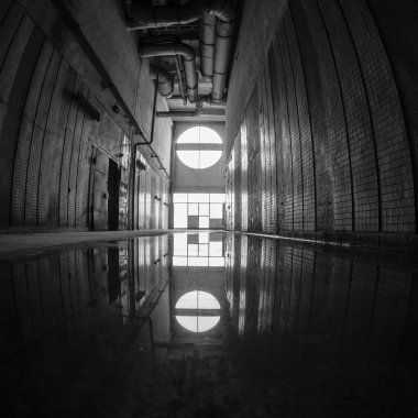 Terk edilmiş eski bir fabrikada karanlık bir koridor. Zeminde, içinin yansıdığı su.