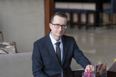 Takım elbiseli gözlüklü bir adamın portresi. Bir adam temiz bir iç mekanda kanepeye oturur.