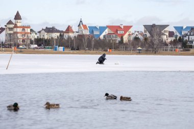 Yalnız bir balıkçı hayatını riske atar, ince eriyen buz ve balıkların kenarında tehlikeli bir şekilde oturur. Ördekler suda yüzer, güzel evler uzak kıyılarda görünür..