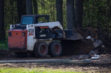 Şehir parkında yapılan çalışmalardan sonra küçük bir yükleyici çöpleri topluyor..