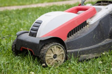 Eski bir plastik elektrikli çim biçme makinesi biçilmiş bir çimlerin üzerinde duruyor.