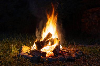 Geceleyin yanan odunları olan renkli bir şenlik ateşi. Çimlerin üzerinde yakacak odun ve taşlarla çevrili şömine.