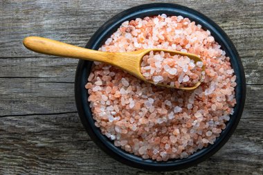 Büyük pembe Himalaya tuzu kristalleriyle dolu yuvarlak bir kara kase. Üstünde bir bambu kaşığı var.
