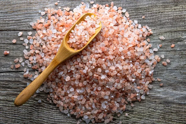 stock image A pile of large crystals of pink himalayan salt on an aged rough board. On top is a bamboo spoon with salt. Good healthy food supplement