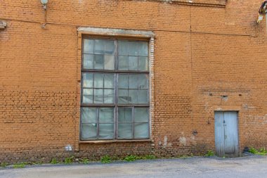 Büyük, eski, harap bir kırmızı tuğla ev, büyük, harap bir pencere ve gri ahşap bir kapı. Terk edilmiş eski bir fabrika..