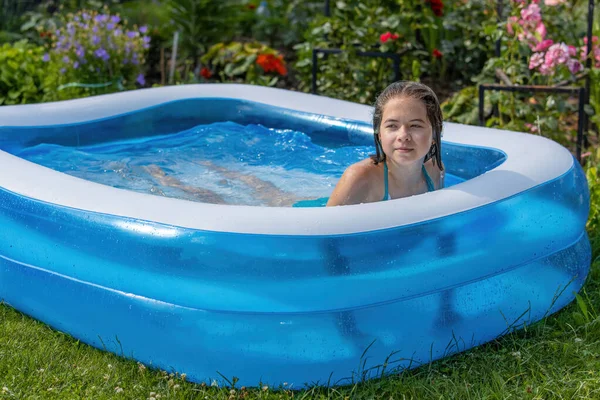 青い水着の女の子が咲く庭の青いインフレータブルプールで入浴 ストック写真