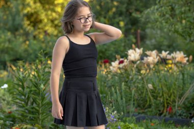 Siyah elbiseli bir kız çiçek açan bir yaz bahçesinde poz veriyor.