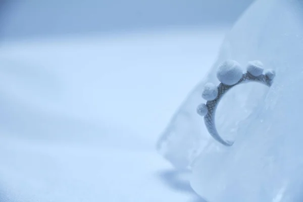 Close up silver ring frozen into ice on white background, selective focus