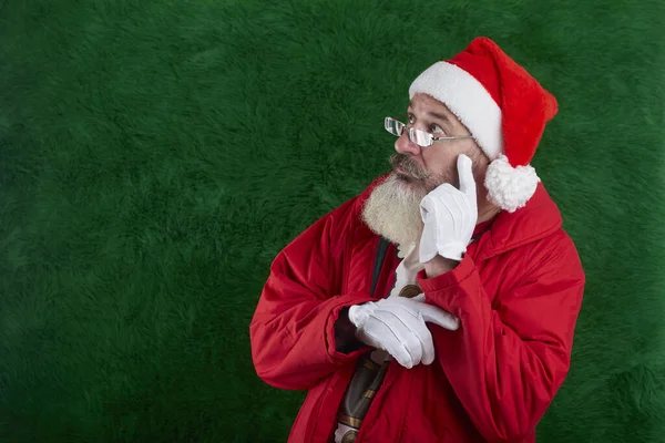 Mature bearded man with eyeglasses on face wearing Santa hat, Santa looks away at something, copy space — 스톡 사진