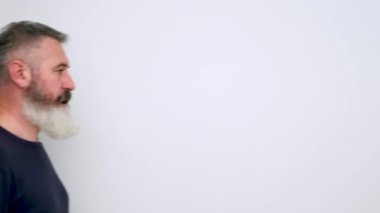 Olgun sakallı adam sola geliyor, kameraya baş parmağını kaldırıyor ve beyaz arka planda yürüyor.