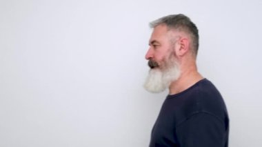 Olgun sakallı bir adam çıkar, kameraya el sallar ve beyaz arka planda yürür.