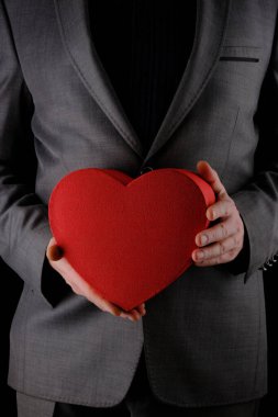 Tanınmayan takım elbiseli adam elinde kalp şeklinde bir hediye kutusu, kırmızı kutu, tebrik konsepti, siyah arka plan