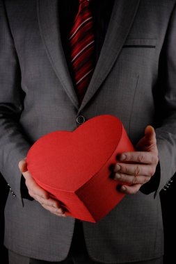 Tanınmayan takım elbiseli adam elinde kalp şeklinde bir hediye kutusu, kırmızı kutu, tebrik konsepti, siyah arka plan