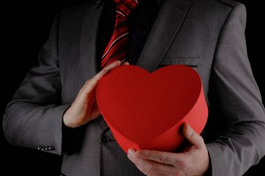 Tanınmayan takım elbiseli adam elinde kalp şeklinde bir hediye kutusu, kırmızı kutu, tebrik konsepti, siyah arka plan