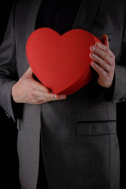 Tanınmayan takım elbiseli adam elinde kalp şeklinde bir hediye kutusu, kırmızı kutu, tebrik konsepti, siyah arka plan