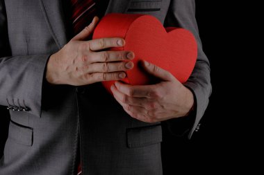 Tanınmayan takım elbiseli adam elinde kalp şeklinde bir hediye kutusu, kırmızı kutu, tebrik konsepti, siyah arka plan