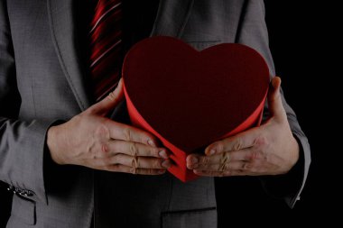 Tanınmayan takım elbiseli adam elinde kalp şeklinde bir hediye kutusu, kırmızı kutu, tebrik konsepti, siyah arka plan