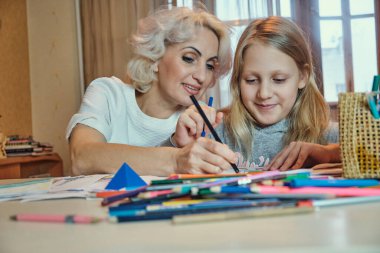 Olgun anne ve kızı birlikte çiziyorlar, evde ödev yapıyorlar, seçici bir şekilde odaklanıyorlar.