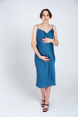 Beyaz gri arka planda mavi elbiseli hamile bir kadının stüdyo portresi, mutlu hamilelik kavramı.