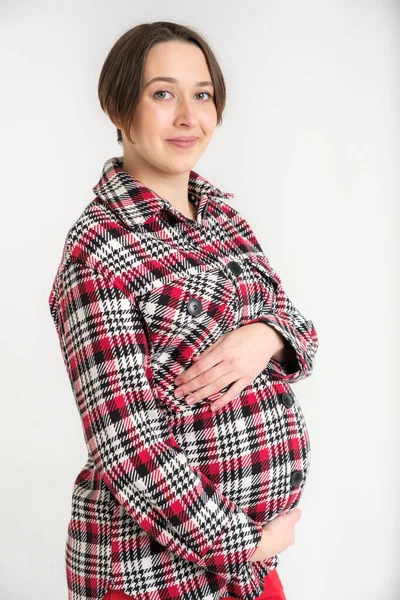 Studio portrait of young adult woman in warm home clothes, happy pregnancy concept, white backdrop
