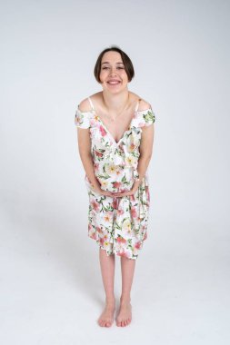 Beyaz gri arka planda, mutlu hamilelik kavramı üzerine yaz elbisesi giymiş neşeli hamile kadının stüdyo portresi.