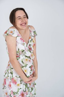 Beyaz gri arka planda, mutlu hamilelik kavramı üzerine yaz elbisesi giymiş neşeli hamile kadının stüdyo portresi.