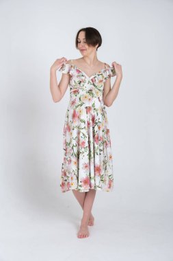 Beyaz gri arka planda, mutlu hamilelik kavramı üzerine yaz elbisesi giymiş neşeli hamile kadının stüdyo portresi.