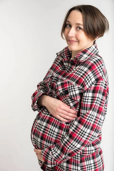 Studioporträt einer jungen erwachsenen Frau in warmer Heimkleidung, Konzept einer glücklichen Schwangerschaft, weißer Hintergrund — Stockfoto