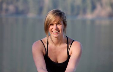 Güzel mutlu kız gölün kenarında poz veriyor. Arkasında göl olan sığ bir alan derinliği var.