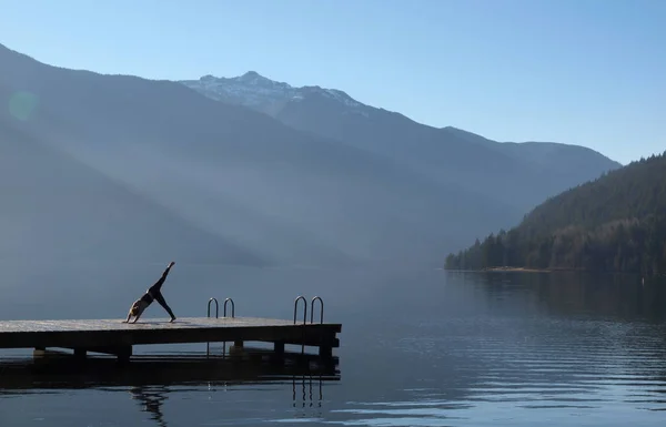 一个女孩在一个码头上练习瑜伽 码头后面有一个雾蒙蒙的库尔图斯湖 — 图库照片