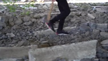 Bir genç elinde baltayla harabelerde yürüyor.