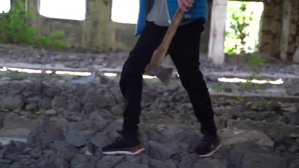 Un adolescent marche avec une hache à travers les ruines — Video