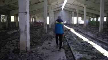 Bir genç elinde baltayla harabelerde yürüyor.