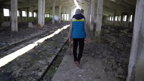 Een tiener loopt met een bijl door de ruïnes — Stockvideo