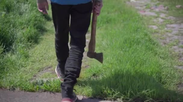 Een tiener loopt met een bijl op een verlaten boerderij — Stockvideo