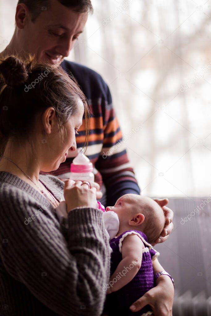 Slav Bulgarian couple with a baby. Father and mother feeding theirs firstborn daughter with a milk bottle. Fathers day and Mothers day