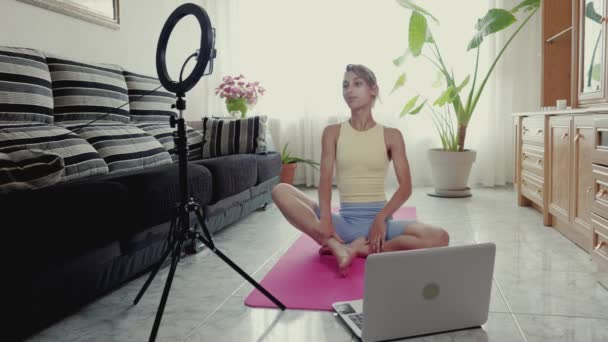 Yoga, Pilates and wellness instructor training κατά τη διάρκεια κλειδώματος στο διαμέρισμά της, live streaming video call. Ισπανόφωνη νεαρή γυναίκα σε απευθείας σύνδεση διδασκαλία με ένα smartphone και φορητό υπολογιστή online μάθημα. — Αρχείο Βίντεο