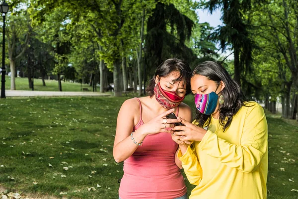 Lesbijki lesbijki piszą SMS-y z technologią smartfona i maską twarzy podczas pandemii. młody żółty i lawendowy. LTBQ — Zdjęcie stockowe