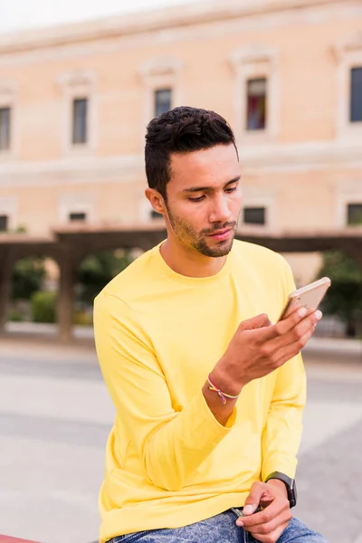 A young latin america man chatting online on smartphone technology. yellow — Stock Photo, Image