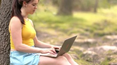 Genç bir kadın parkta dizüstü bilgisayarla ders çalışıyor. Okul uzaklığı eğitim üniversitesine.