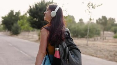 Üniversite kampüsündeki beyaz bir kadın, akıllı telefonuyla kulaklıkla müzik dinliyor.