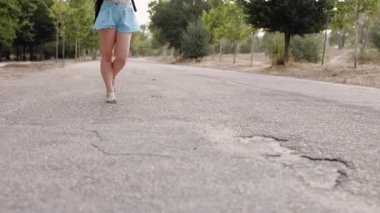 Üniversite kampüsündeki beyaz bir kadın, akıllı telefonuyla kulaklıkla müzik dinliyor.